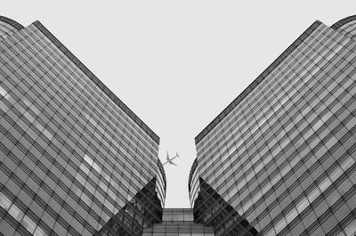 Low angle view of plane flying between modern building