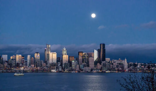 Sea by modern buildings against sky at night