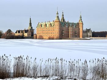 Frozen river by buildings against sky