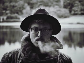 Portrait of man exhaling smoke against lake