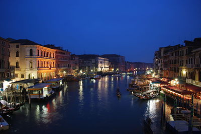 Boats moored in river in front of illuminated city at night