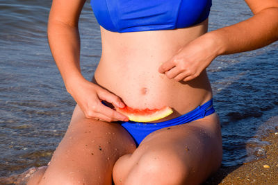 Midsection of woman in bikini holding watermelon on beach