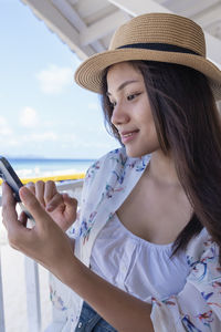 Young woman using smartphone by seaside. happy tourist relaxing and using mobile phone for social 
