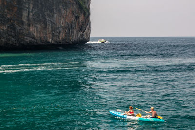 People kayaking on sea against sky