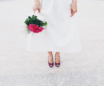 Low section of bride holding rose bouquet while standing on textured floor