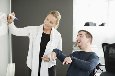 Businesswoman writing on whiteboard while working with disabled businessman in office