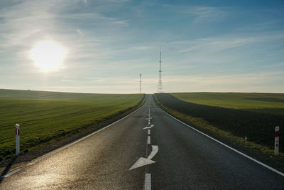 Empty road amidst field against sky