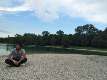 Man sitting on riverbank against sky