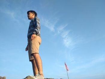 Low angle view of young man standing against blue sky