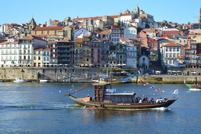 Sailboats in river by buildings in city against clear sky