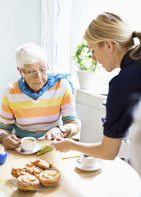 Female caretaker examining senior woman's finger at breakfast table in nursing home