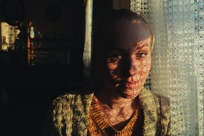 Close-up portrait of woman by window with shadow