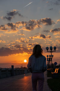 Rear view of man standing at beach against sky during sunset