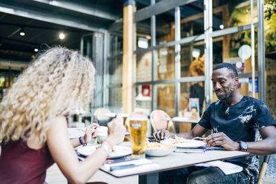 Blond woman and african man enjoy eating in restaurant.