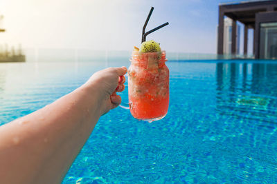 Midsection of person holding drink at swimming pool
