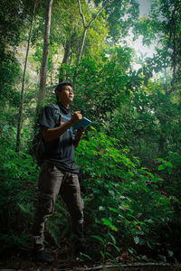 Full length of man holding camera in forest