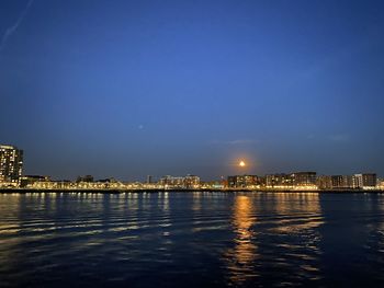 Illuminated city by sea against sky at night