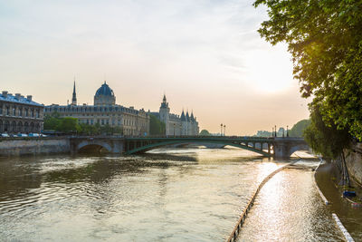 Conciergerie by river and bridge in city against sky during sunset