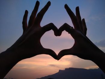 Cropped silhouette hands making heart shape against sky during sunset