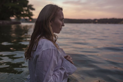 Side view of woman standing by lake during sunset