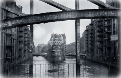 Bridge over river by buildings against sky