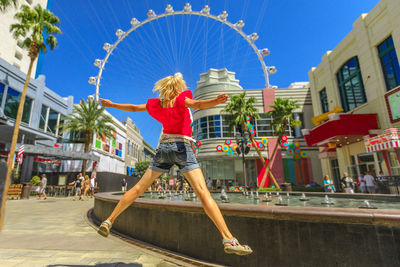 Woman with ferris wheel in city against blue sky
