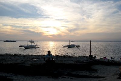 Boy at beach against sky during sunset