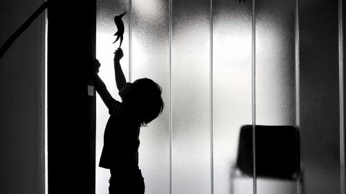 Silhouette boy with arms raised standing in room
