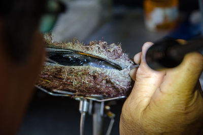 Cropped image of man opening seashell at workshop