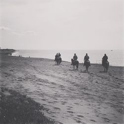 People riding on beach against clear sky