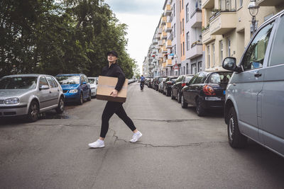 Side view of delivery woman with cardboard box walking on street in city