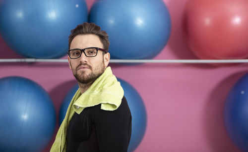 Portrait of man wearing eyeglasses standing against fitness balls