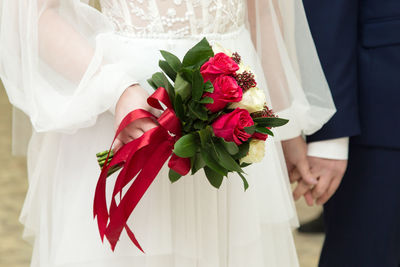 A bright bouquet with red roses in the hands of the bride on the background of a white dress.
