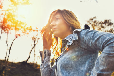 Portrait of young woman looking away against sky during sunset