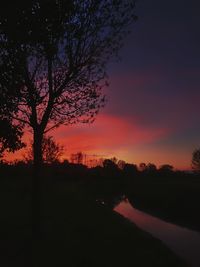 Silhouette trees on field against romantic sky at sunset