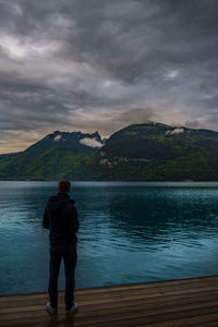 Rear view of man looking at lake against mountain range