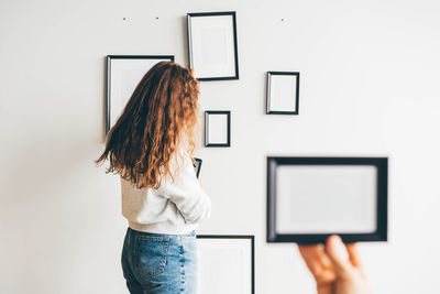 Rear view of woman using digital tablet against wall