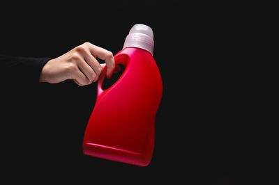 Cropped hand holding bottle against black background