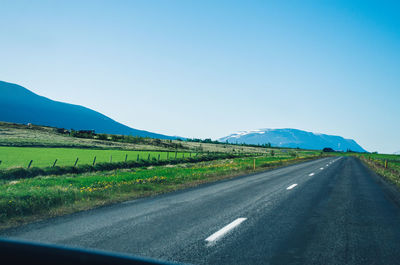 Road amidst field against clear blue sky