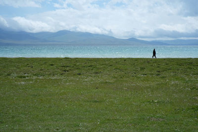 Distant view of man walking at shore against cloudy sky