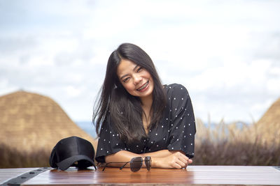 Portrait of young woman sitting against sky