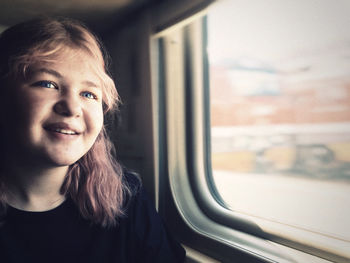 Smiling teenage girl sitting by window in train