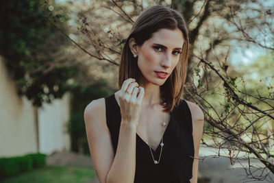 Portrait of young woman standing against tree