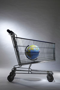 Globe in shopping cart against white wall