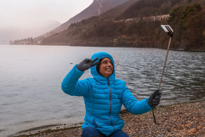 Portrait of smiling young woman standing on lake against sky