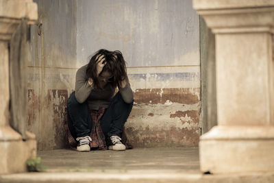 Frustrated young woman sitting outside old building