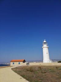 Lighthouse by building against clear blue sky