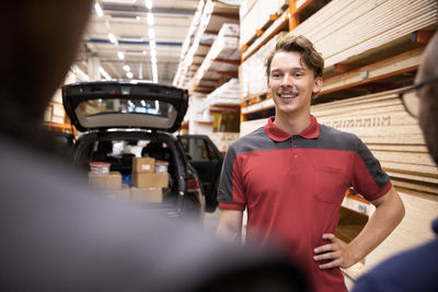 Smiling salesman with hand on hip talking with customer at hardware store