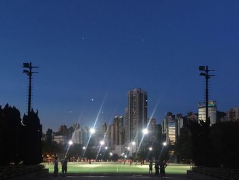 People on illuminated city against blue sky