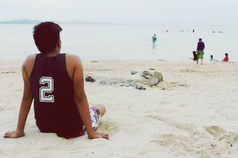 REAR VIEW OF SHIRTLESS MAN HOLDING SANDY BEACH